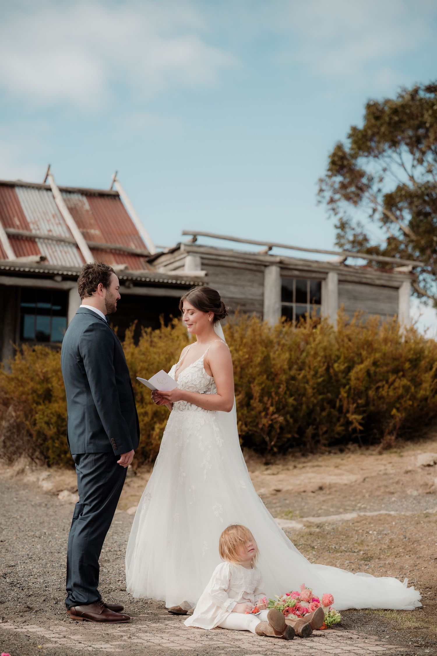 A couple shares a tender moment together outdoors in front of rustic buildings during their wedding photoshoot.
