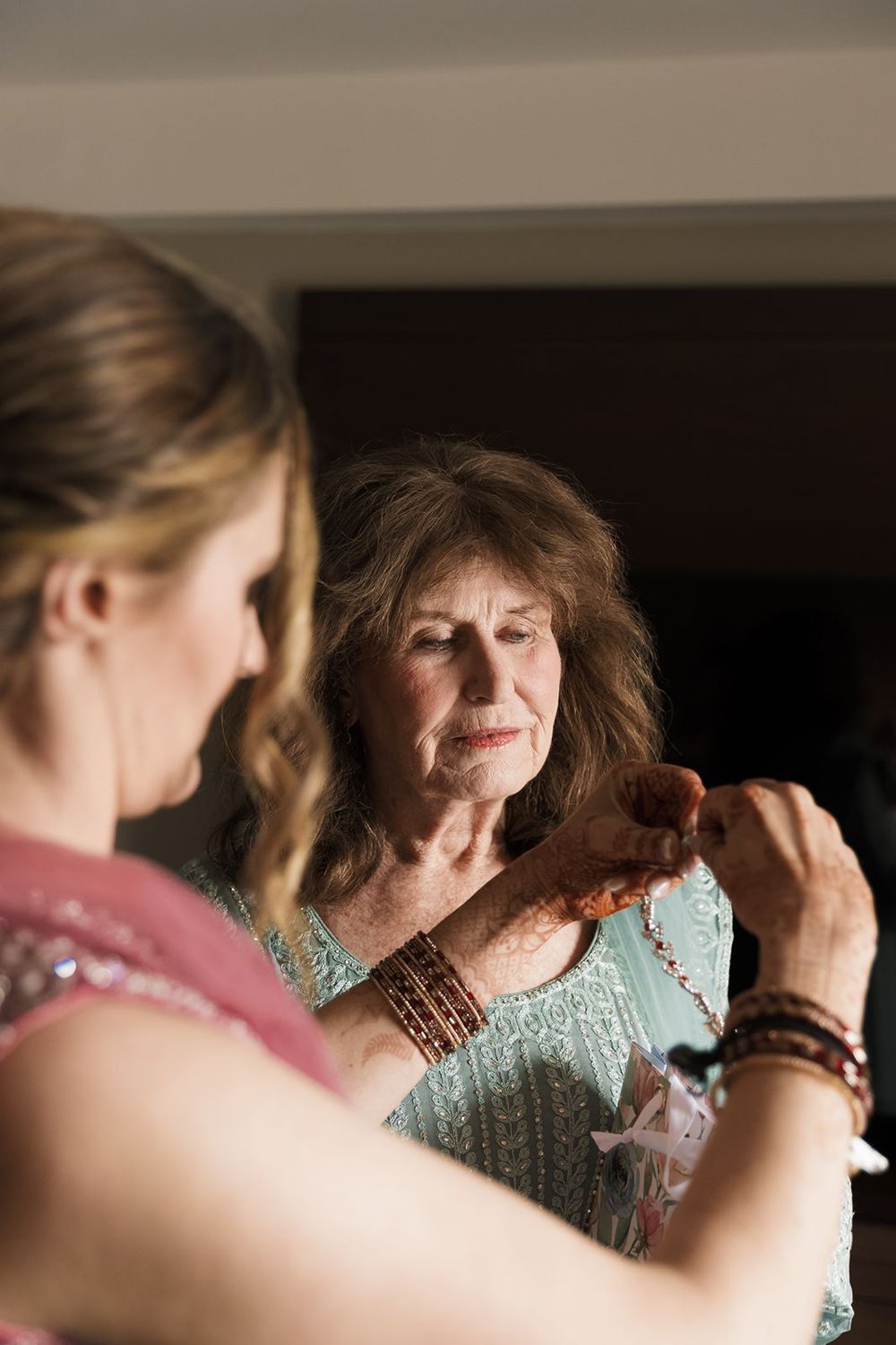 Older woman examines intricate henna bracelet jewelry held by younger woman during wedding preparations.