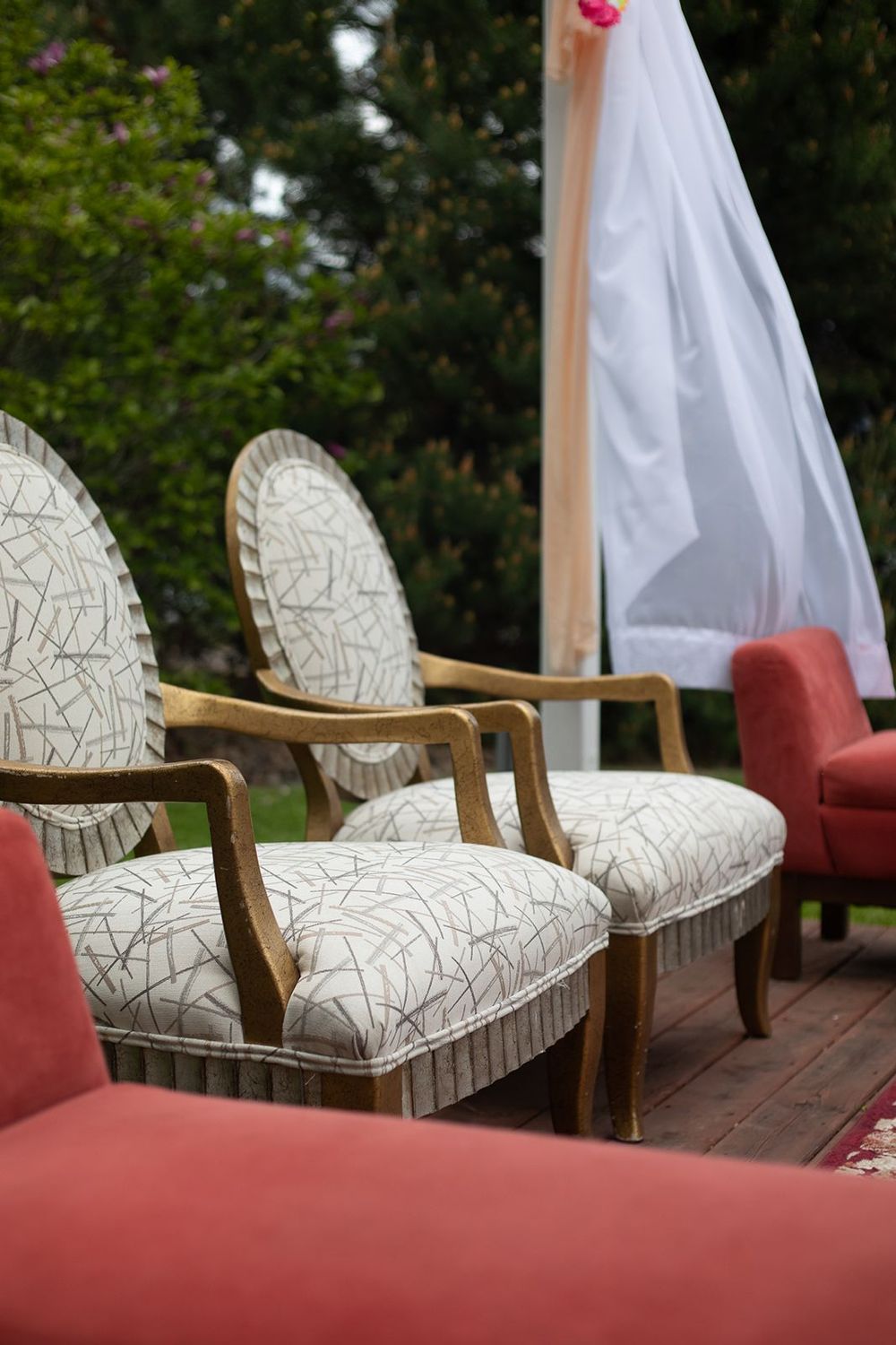 Elegant vintage white and gold armchairs arranged outdoors for a wedding ceremony.