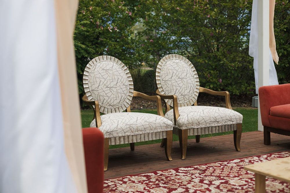 Two ornate white upholstered chairs with gold frames set up for an outdoor wedding.