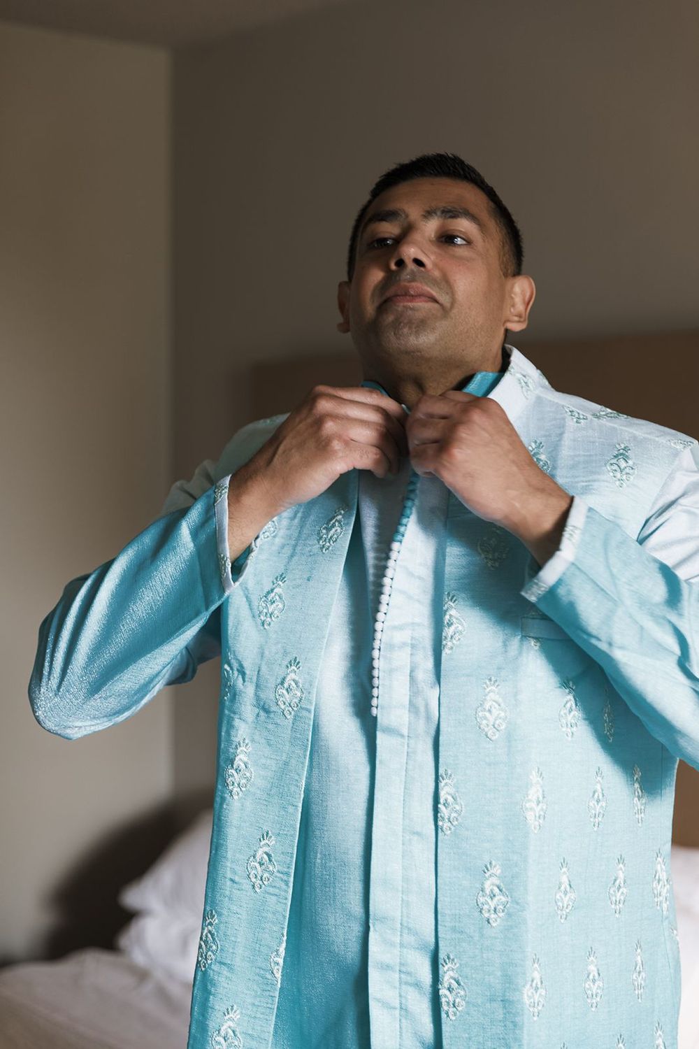 A man adjusting his light blue embroidered kurta while getting ready for a wedding.