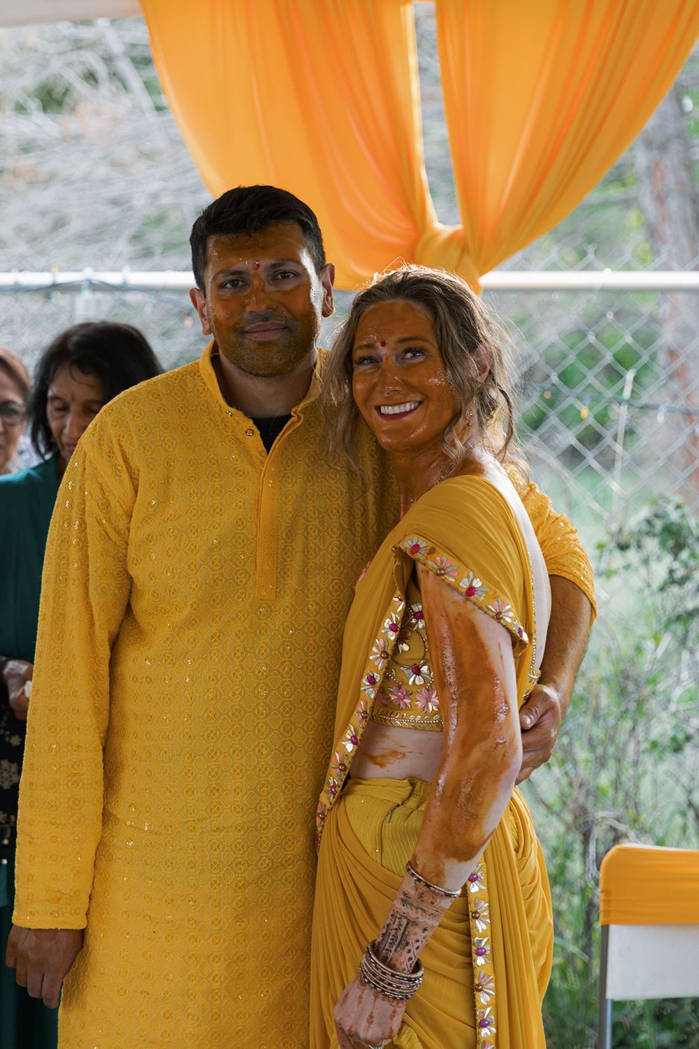 Couple smiling together in matching yellow outfits during Indian Haldi wedding ceremony.
