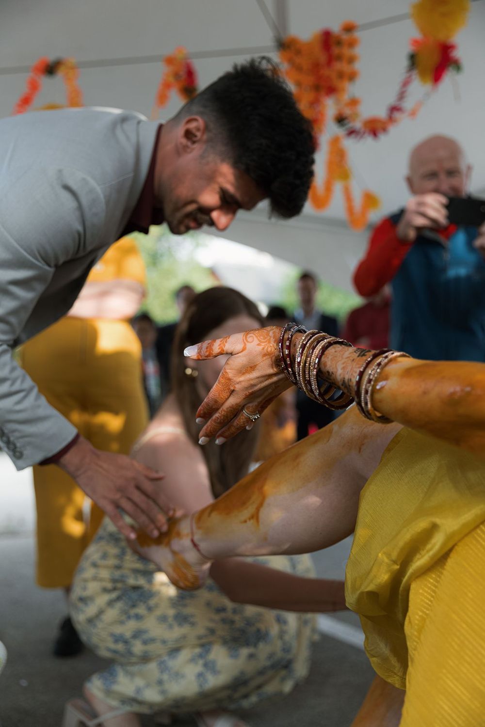 Guest applying turmeric paste to bride's arm during traditional Indian Haldi wedding ceremony.
