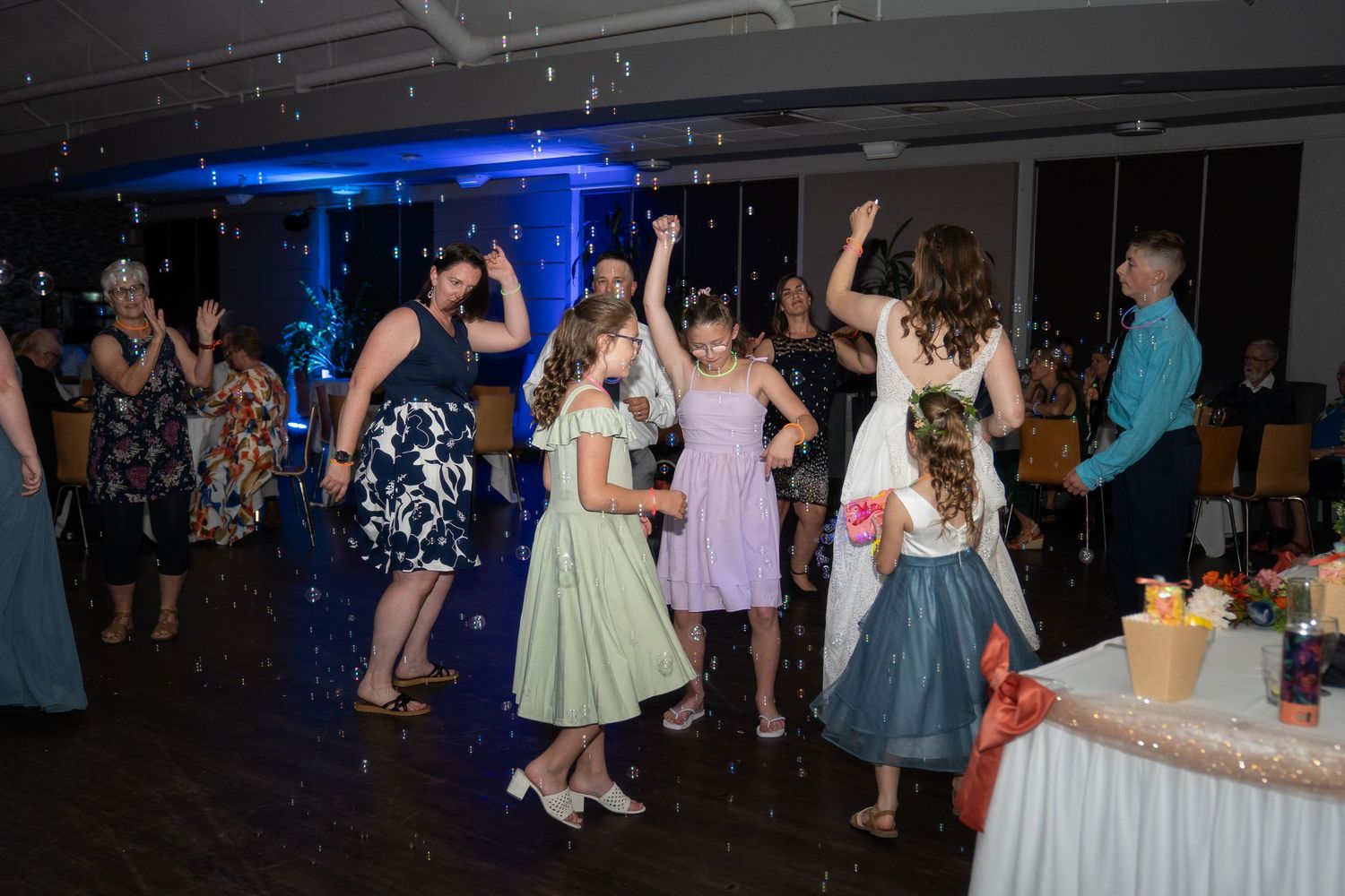 People dancing at a formal event with blue lighting and retro-style dresses in a dark venue.