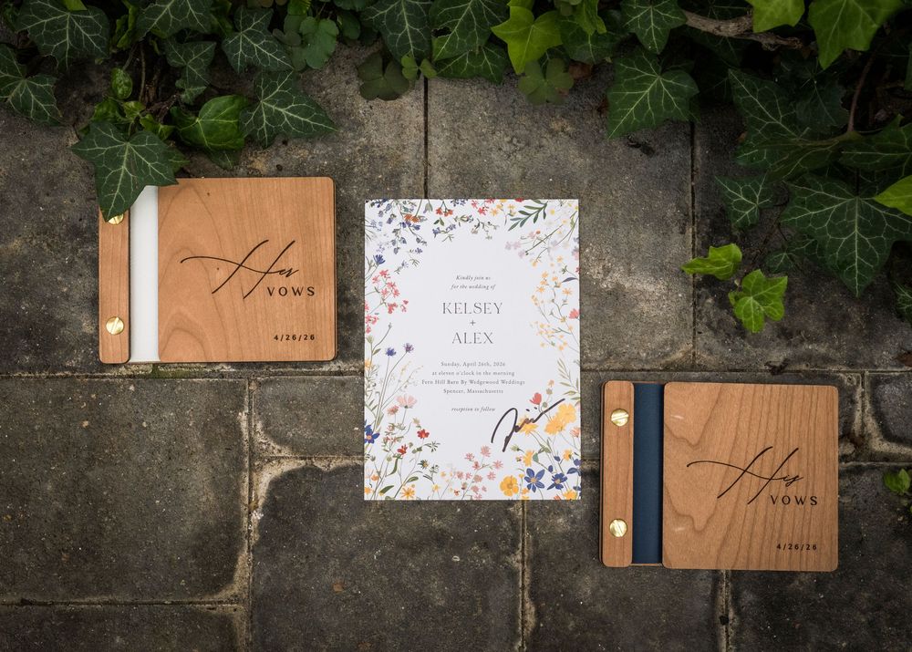 Elegant wedding stationery with floral invitation and wooden vow booklets displayed on stone pavers with ivy.