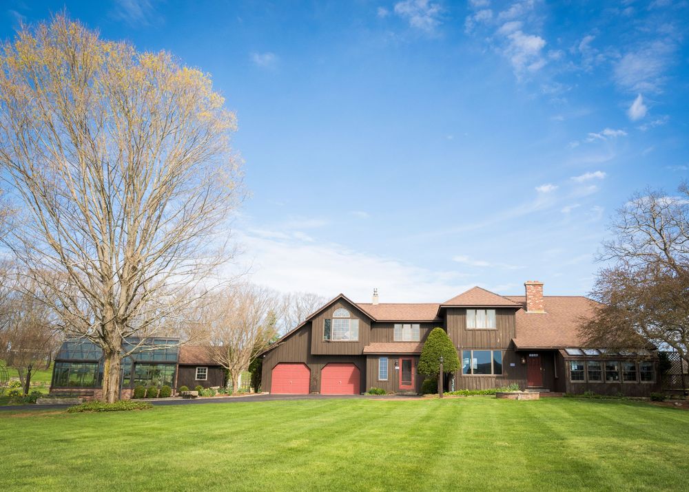 Charming rustic farmhouse wedding venue with red garage doors and lush green lawn under blue sky.