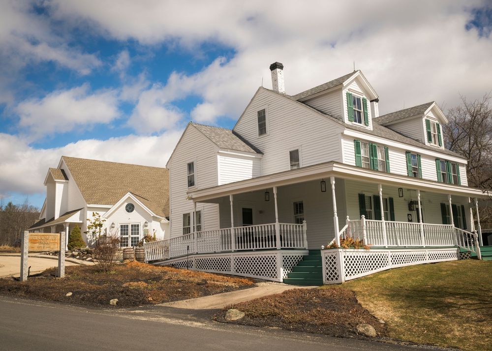 A series of white Cape Cod style houses with green shutters sit along a hillside under partly cloudy skies.
