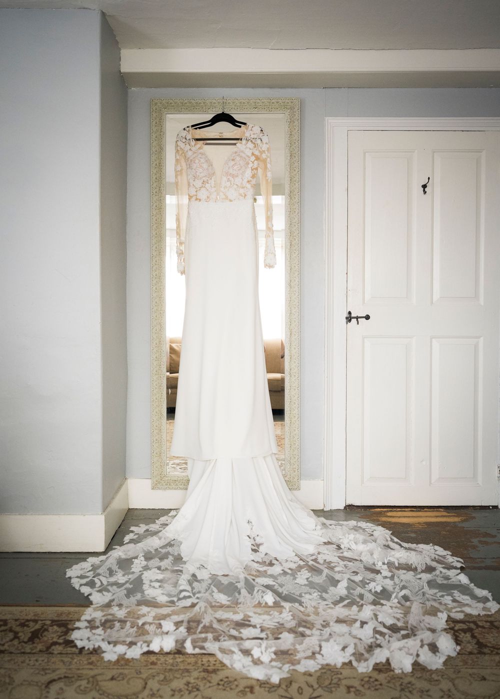 A white wedding dress with a long flowing train displayed against white doors in natural window light.