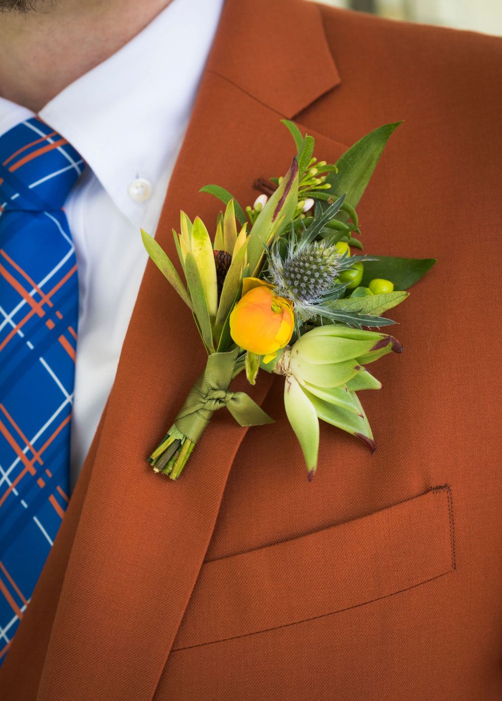 Wedding boutonnieres with yellow flowers and greenery pinned to brown suit jackets.