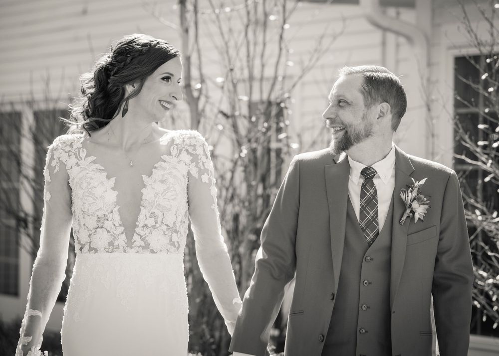 Wedding party poses outdoors against white building in formal attire.