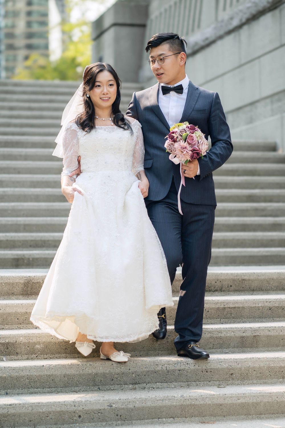 Wedding couple posing on urban concrete steps in traditional formal attire.