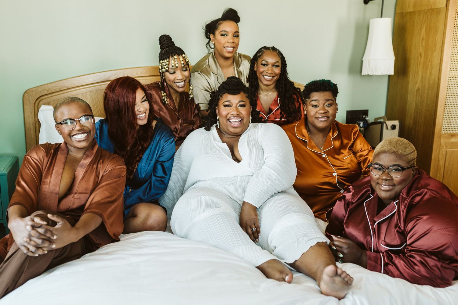 A group of people sitting together on a bed, smiling and laughing in a casual indoor setting.