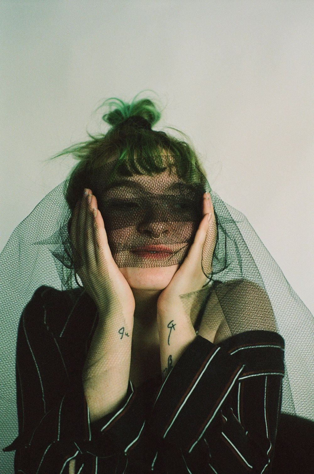 Artistic editorial portraits with hands covering face through green veil and striped dark clothing.