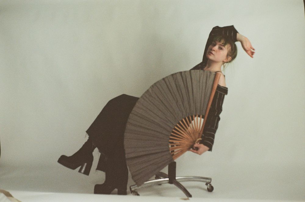 Stylized editorial portraits with dark fan prop and office chair against neutral background.