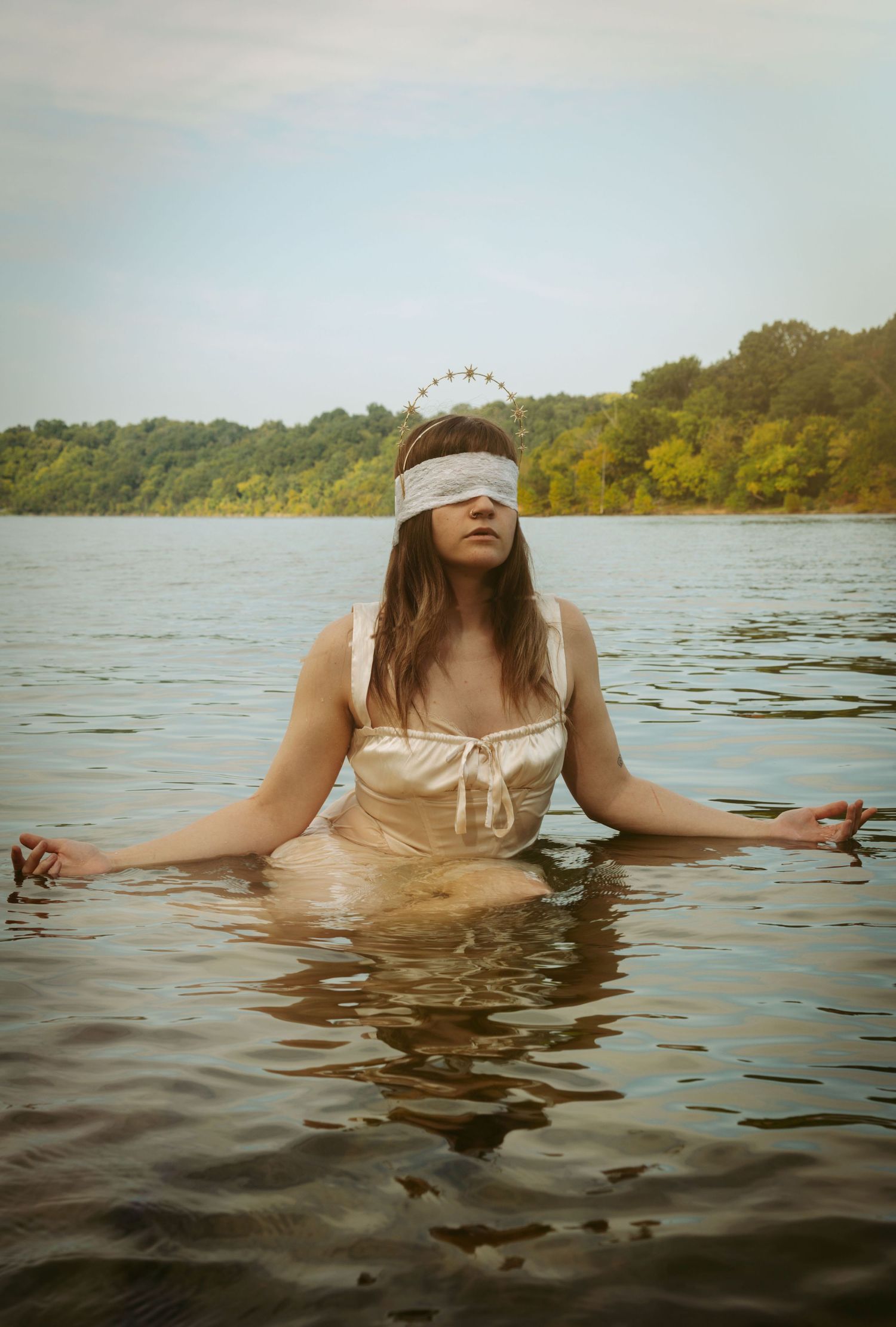 Figure in a light dress floating in calm lake waters with a distant shoreline.