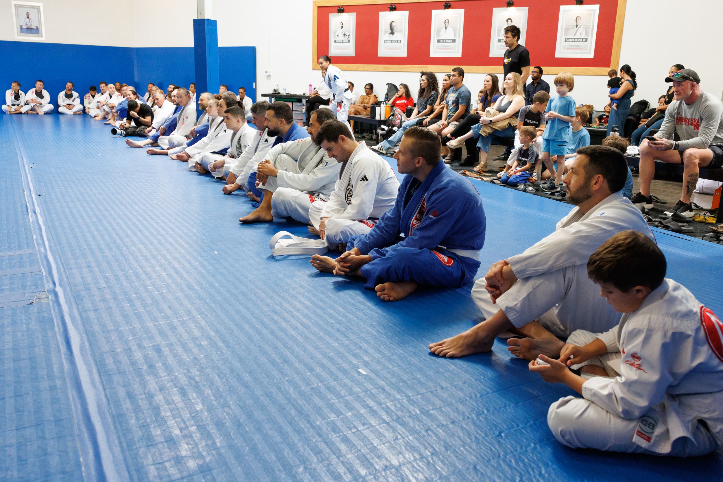 Students sitting in rows on blue mats during a martial arts class.
