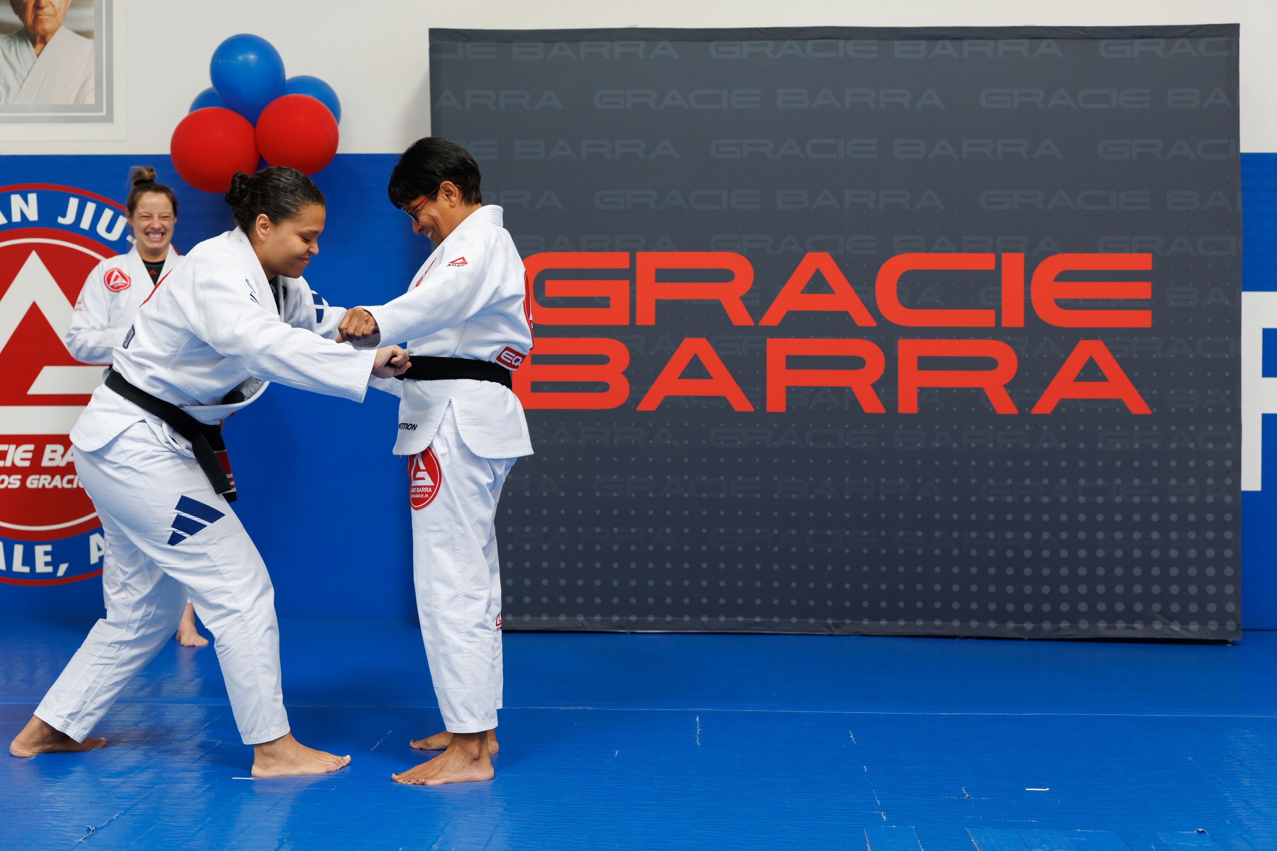 Martial arts practitioners sparring on blue mats in a training facility.