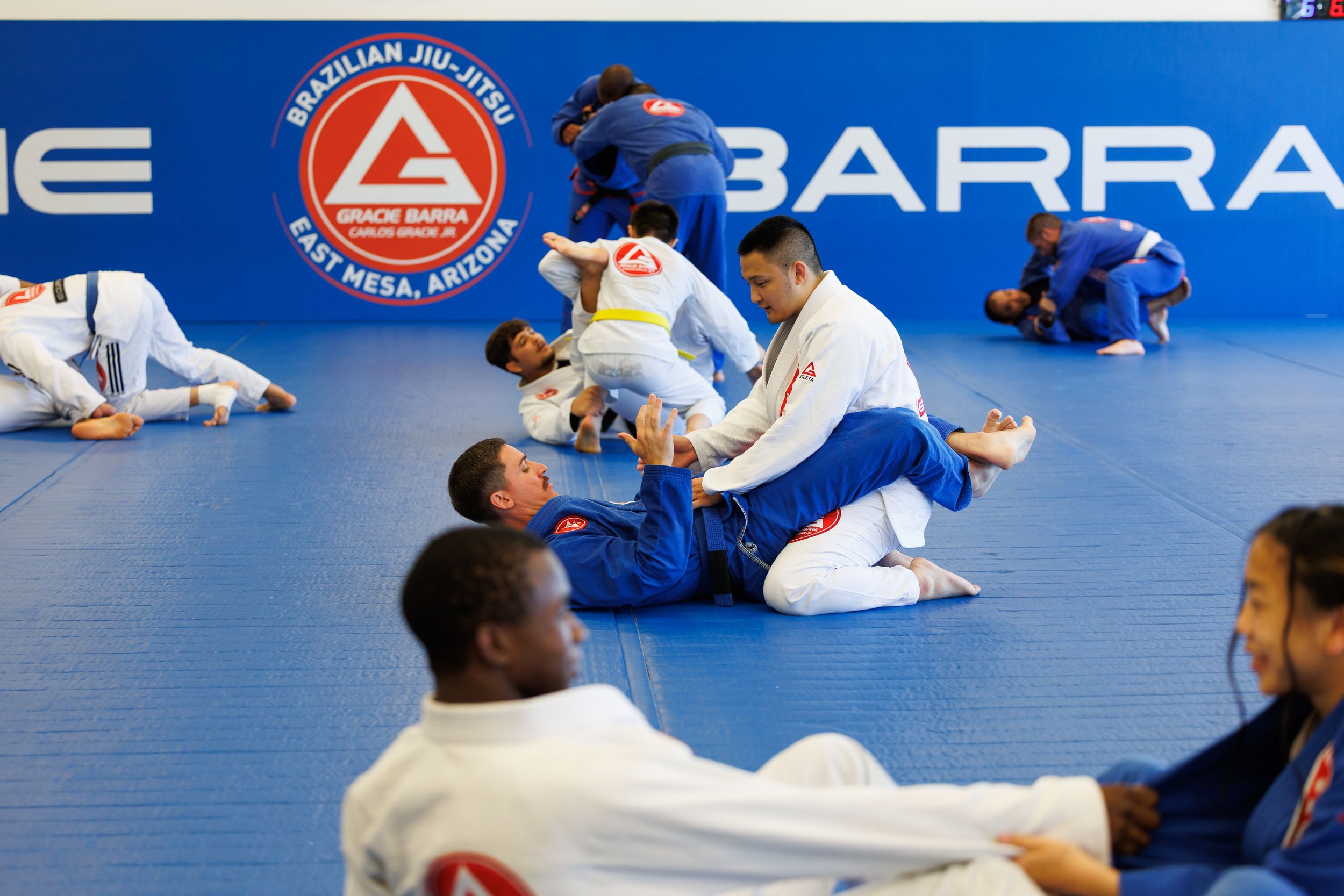 Martial arts students training in a modern facility with blue mats and branded walls.