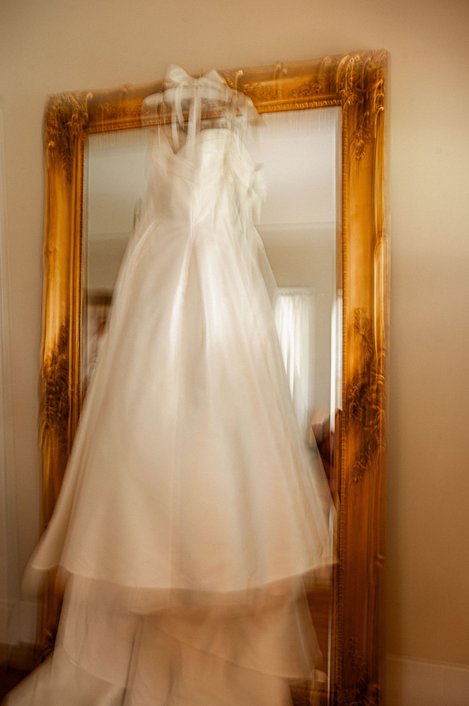 Wedding dress hanging against ornate gold-framed mirrors creating an ethereal motion blur effect.