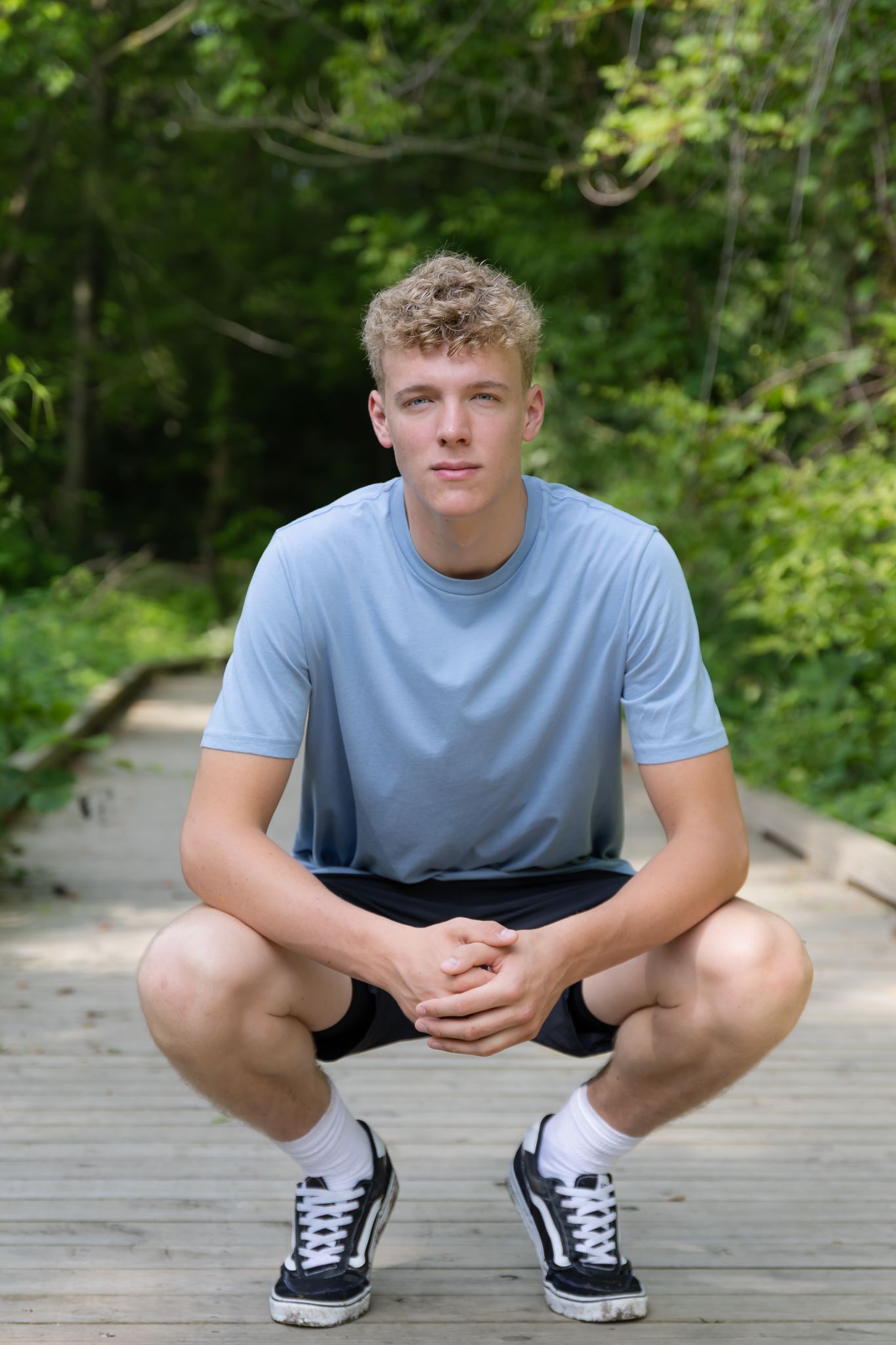 Senior boy is squatting and posing for a senior photo at Draper-Houston Meadows Preserve in Milan, MI.
