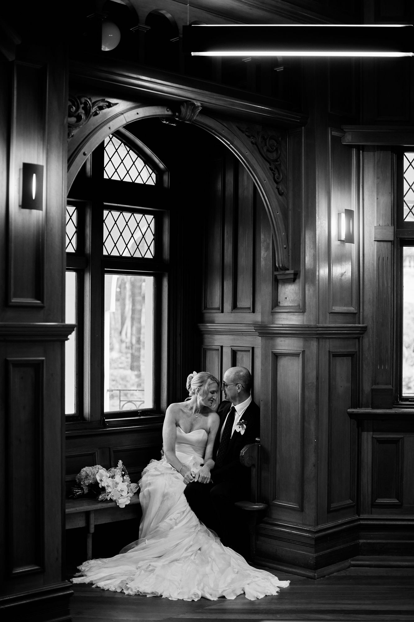A couple in wedding attire walks together along a brick building exterior while sharing a joyful moment.