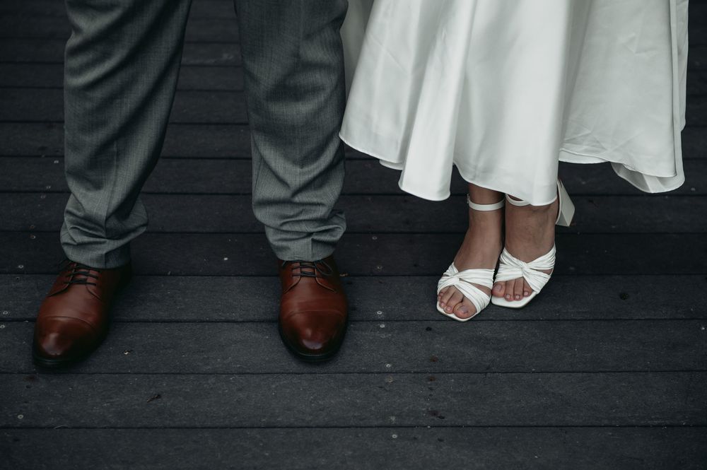 A row of formal shoes and sandals worn by wedding party members standing on a dark wooden floor.