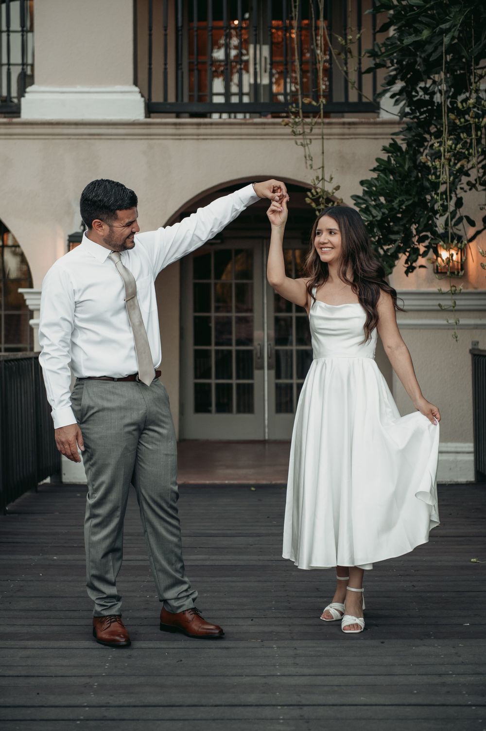 A couple in wedding attire dances together on a wooden deck in a romantic sequence of dance moves.