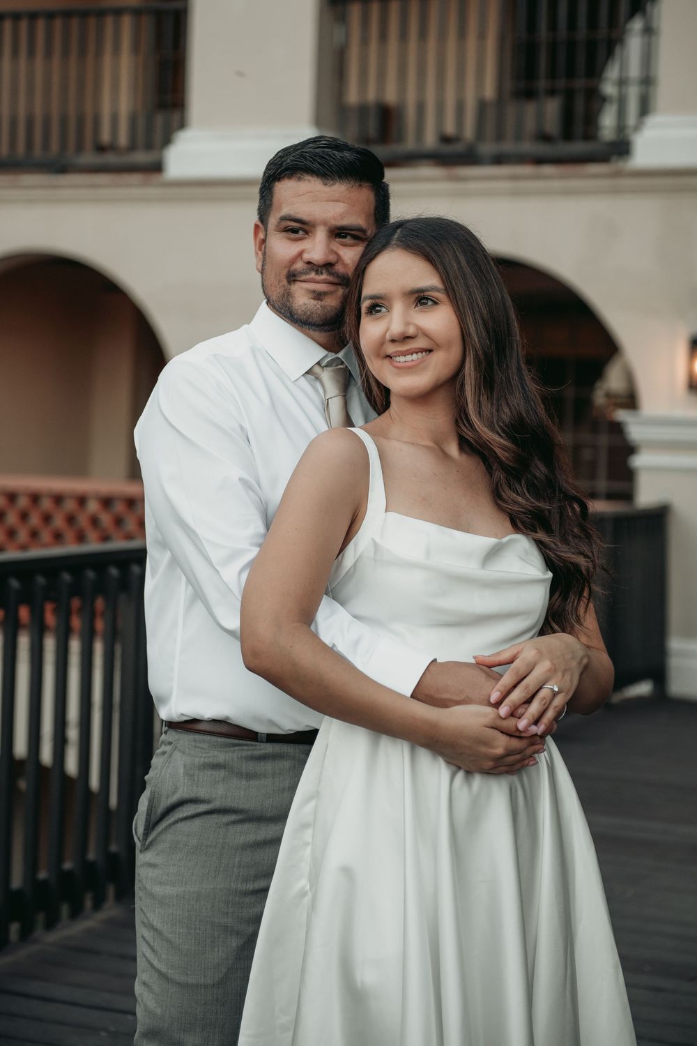 Romantic engagement photos showing a couple embracing in white and grey attire on a balcony.