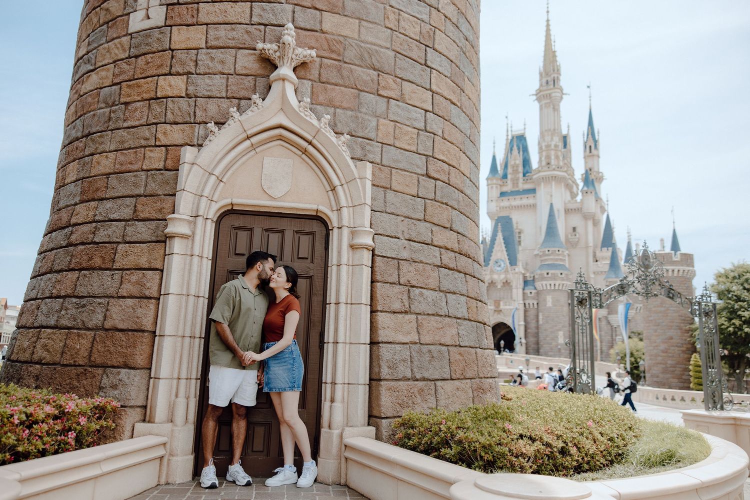 Two people share a romantic moment in a castle doorway with Disney's Cinderella Castle visible in the background.