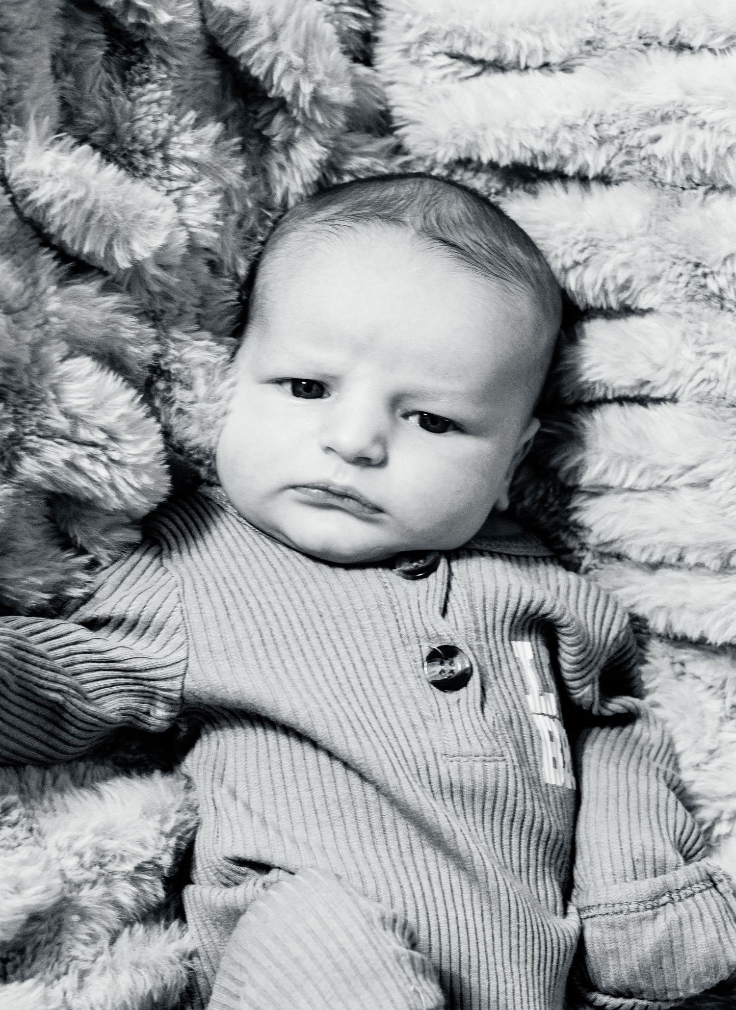 Black and white portrait of a baby wearing a ribbed sweater lying on a textured blanket.