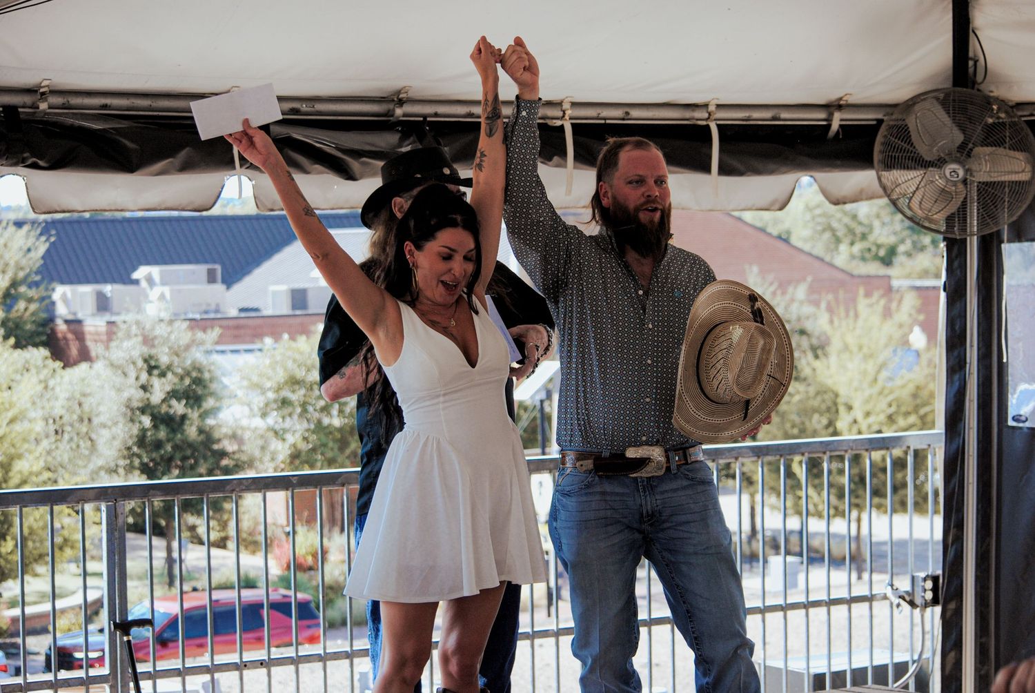 A couple celebrates joyfully with raised arms under a covered outdoor venue during a special occasion.