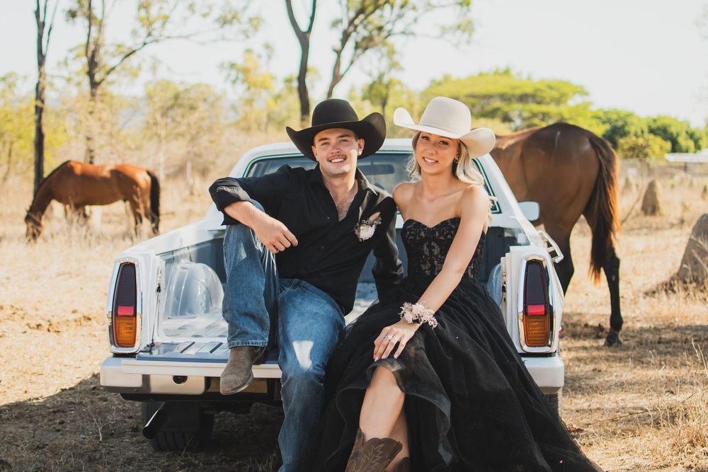 A couple relaxes together in a rustic outdoor setting with horses grazing in the background.