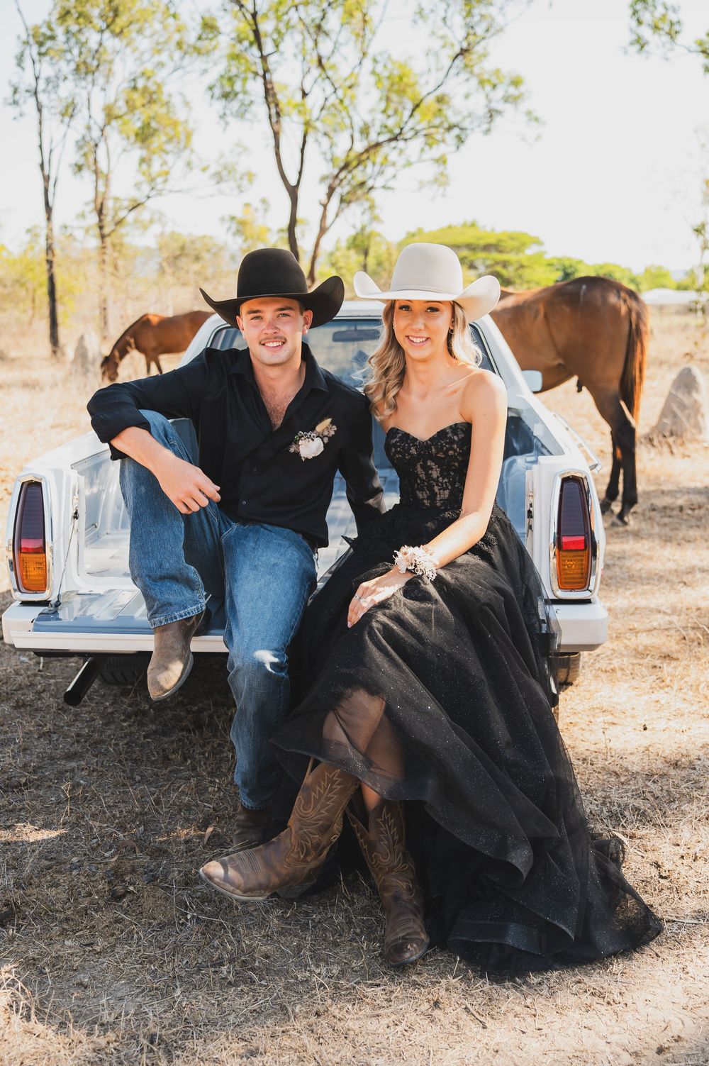 A rustic country photoshoot featuring a pickup truck tailgate and horses in the background.