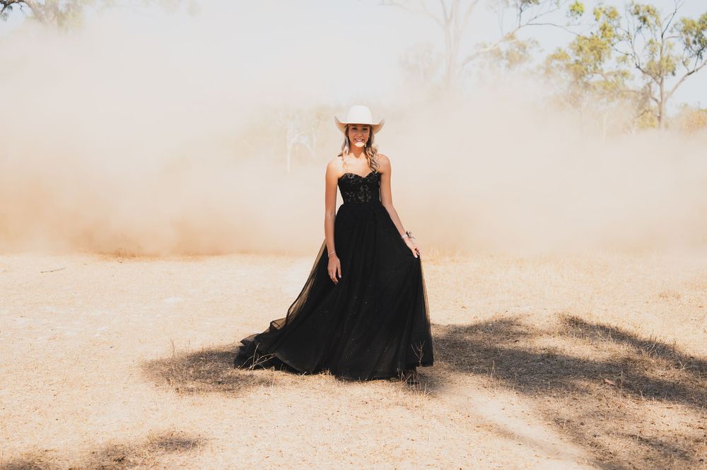 A dramatic black ball gown creates contrast against a dusty outdoor setting with golden lighting.