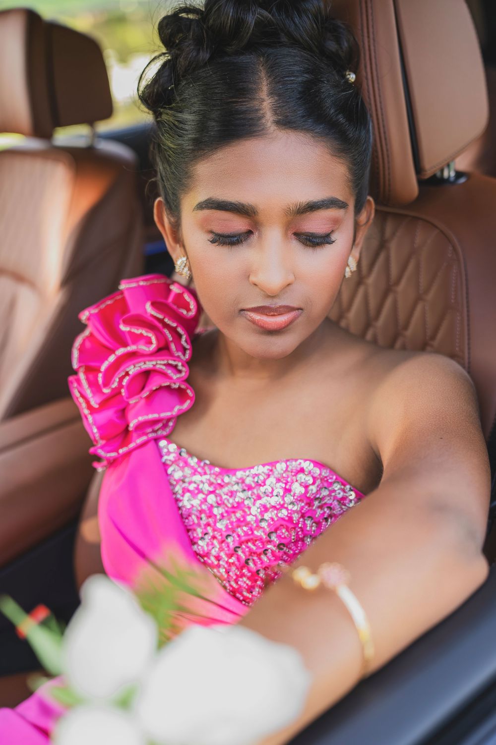 Close up detail of a bright pink sequined dress with ruffled shoulder detail in a car interior.