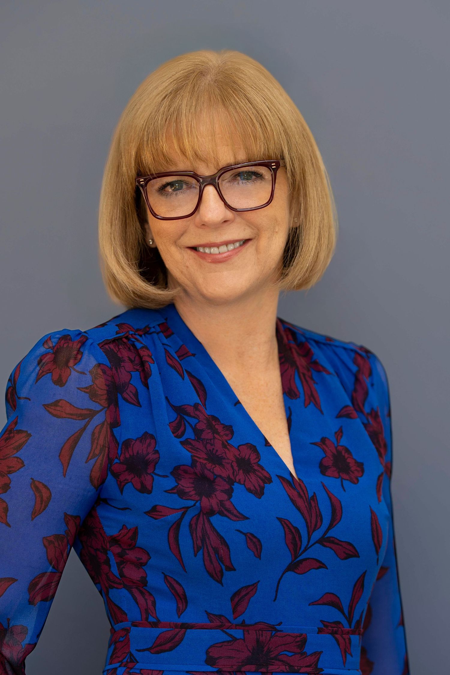 Professional headshot of a woman standing in front of studio backdrop with glasses on.