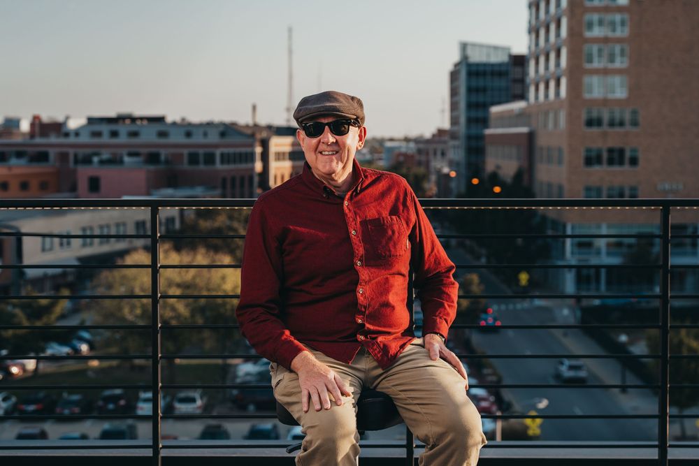 Person in red jacket sitting on rooftop railing with city view.