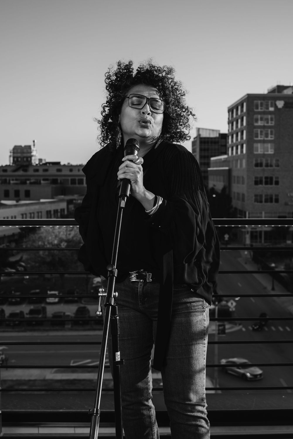 Black and white portrait of a performer with microphone on urban rooftop.