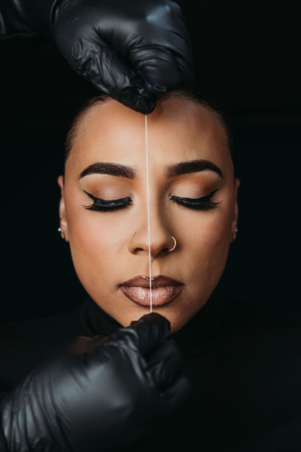 Close-up beauty portrait showing dramatic makeup with closed eyes and black gloves against dark background.