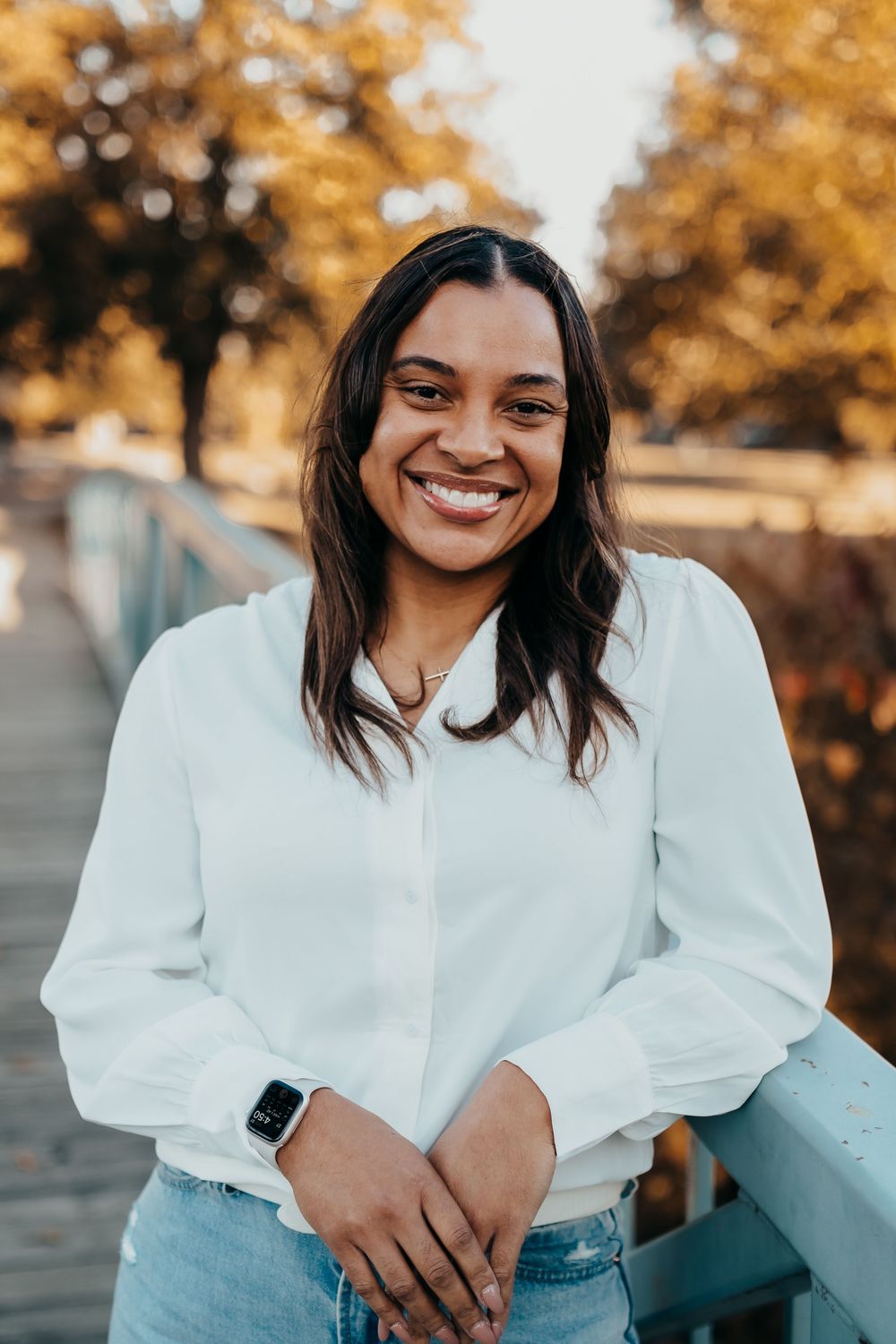 Person in white button-down shirt and jeans smiling outdoors during golden hour.