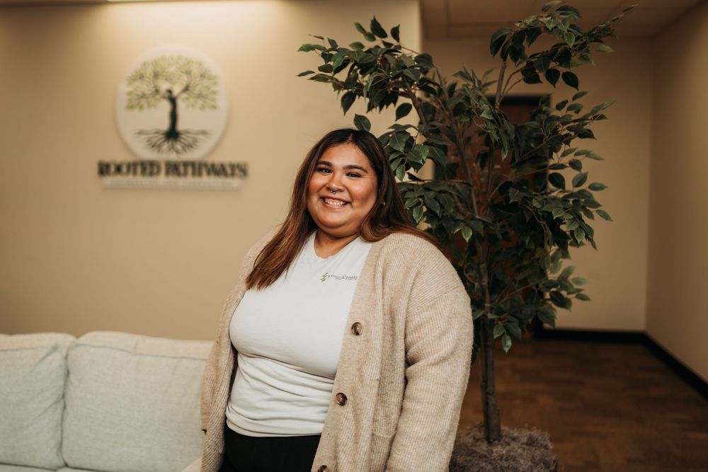 Professional portrait in an office setting with a beige cardigan and indoor plants.