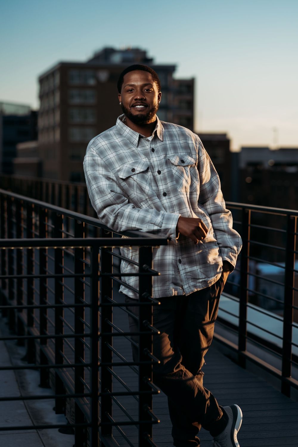 Person in plaid shirt leaning on rooftop railing during sunset.