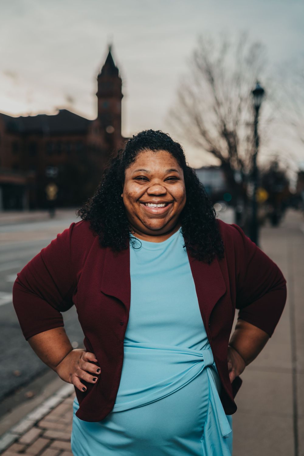 A person in a burgundy jacket and blue shirt poses confidently outdoors. Headshot for lawyer.