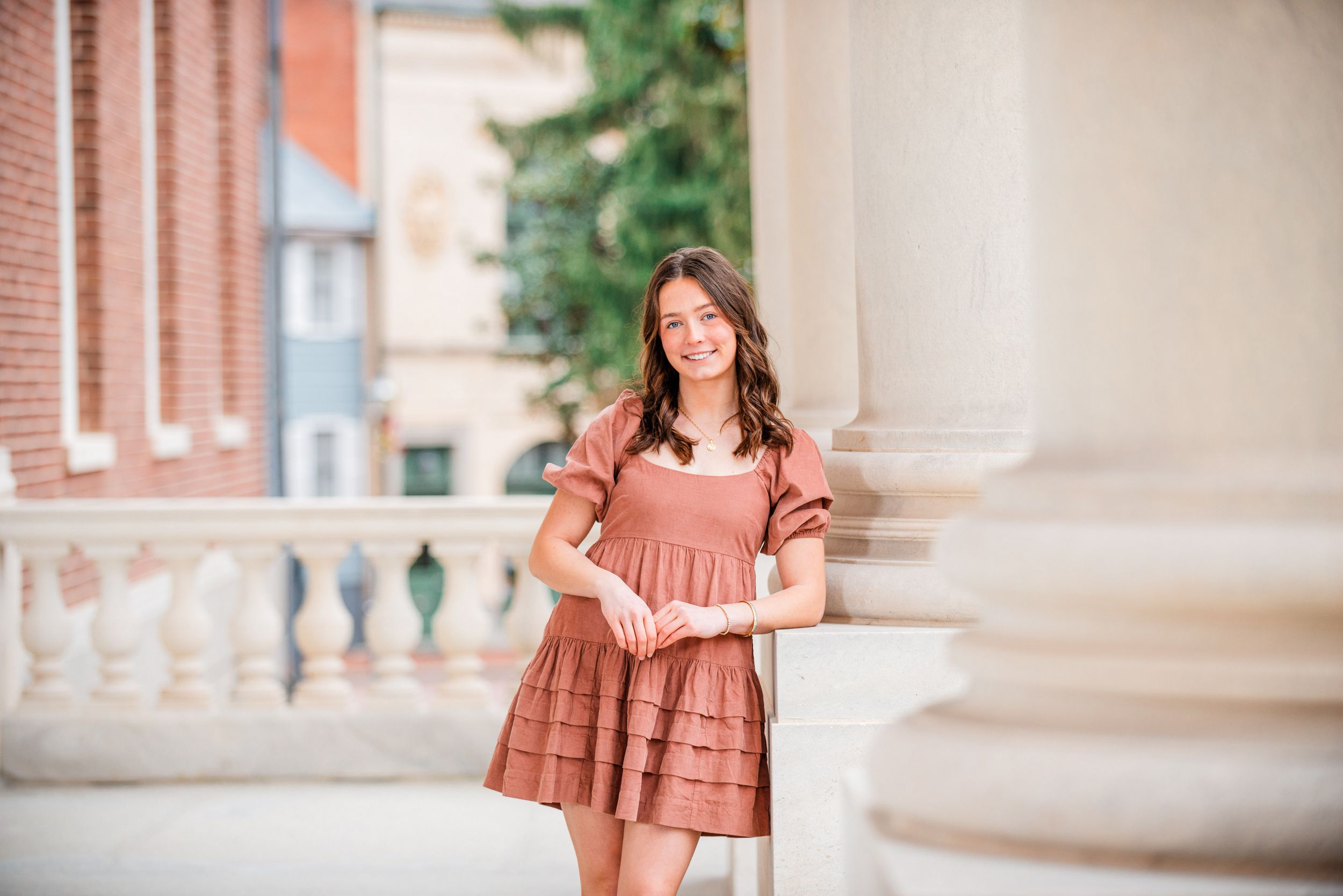 Woman in coral dress poses in front of brick columns during outdoor portrait session.