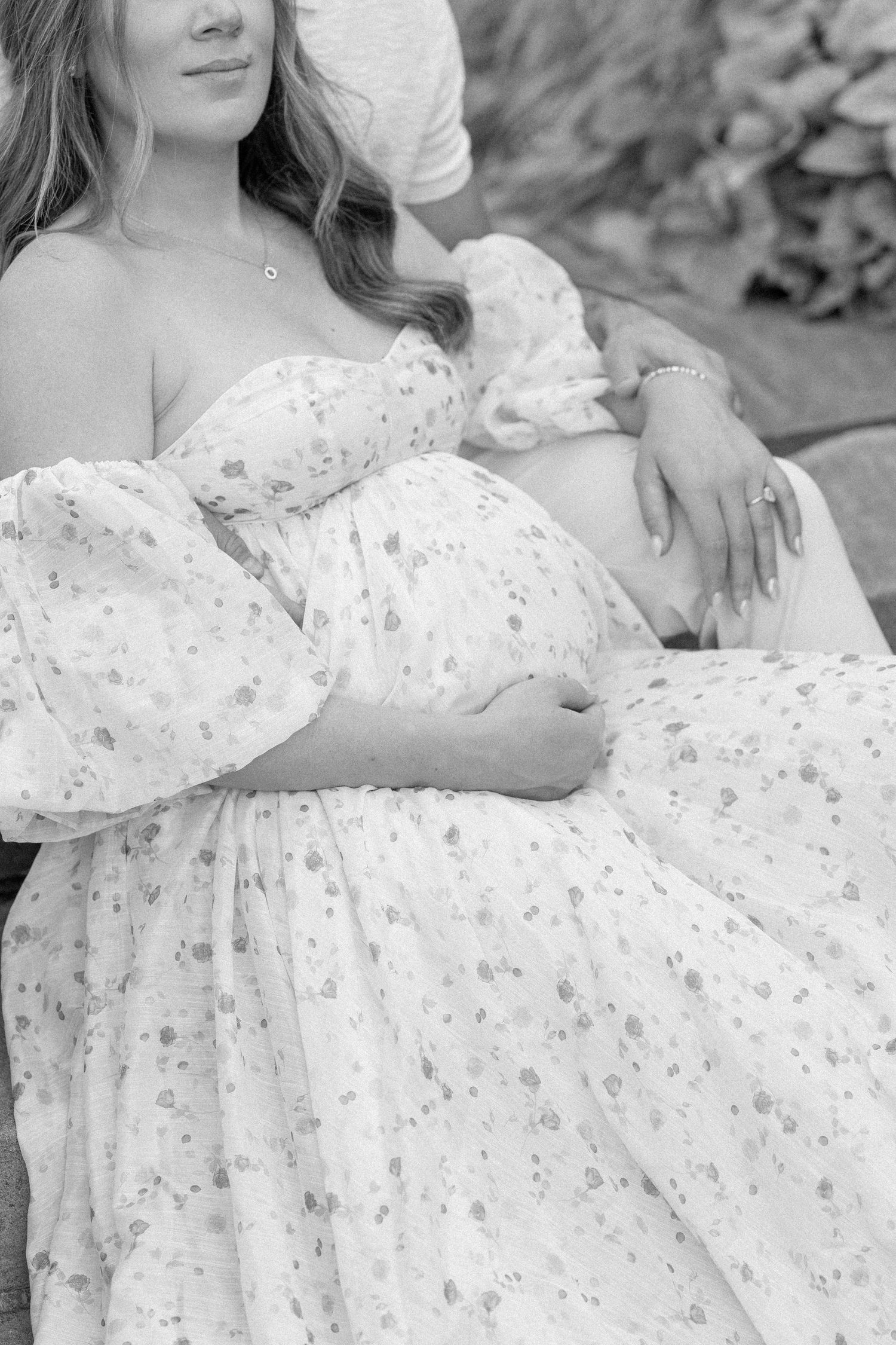 A person wearing a flowing white lace dress poses gracefully on the ground in a black and white photograph.