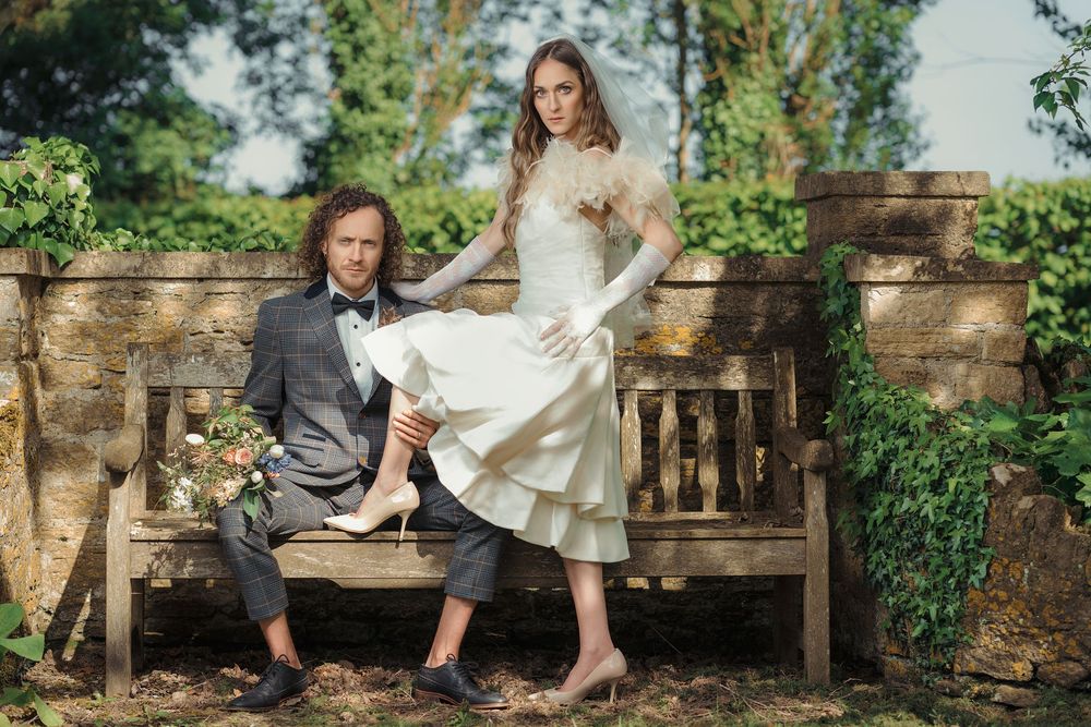 Two people sit together on a rustic wooden bench in a lush garden setting.