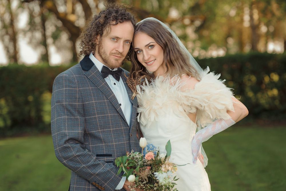 A couple in wedding attire embraces outdoors during an autumn photoshoot with warm natural lighting.