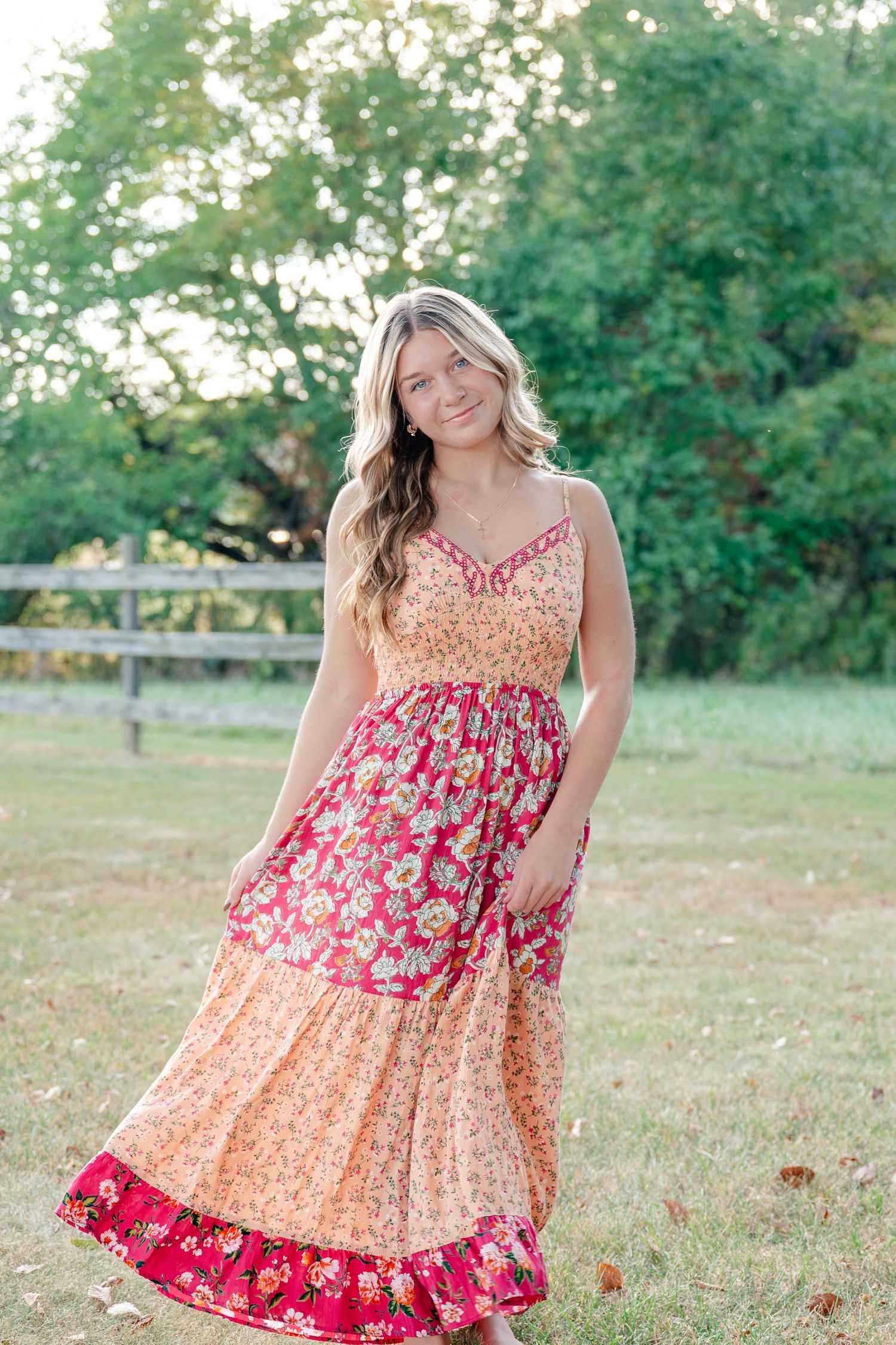 Floral sundress in pink and peach tones photographed in a grassy outdoor setting during golden hour.