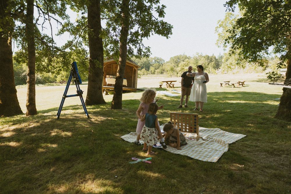 People enjoying a summer day under shady trees at a park with picnic blankets spread out on the grass.