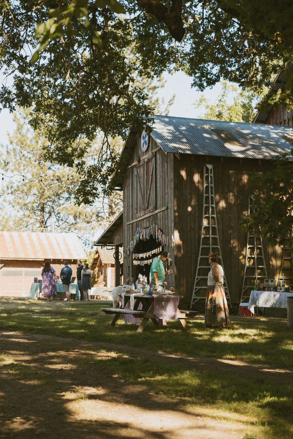 A rustic wooden barn with decorative banners and string lights set up for an outdoor event in a grassy field.